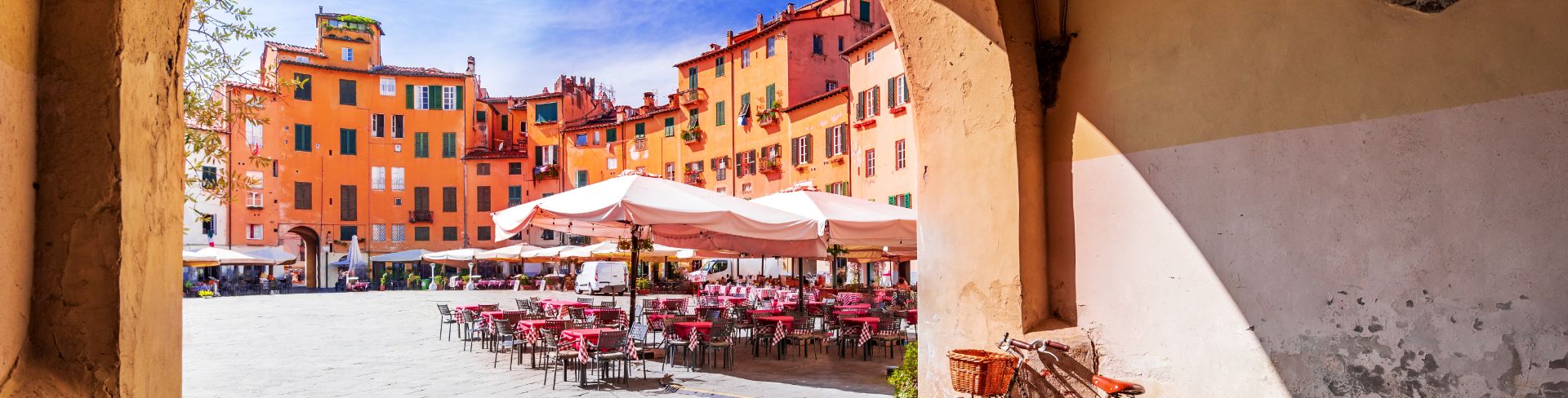 An archway reveals a sun drenched square filled with restaurants. 