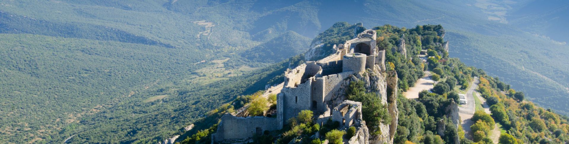 A castle sits atop the peak of a forested mountain. 