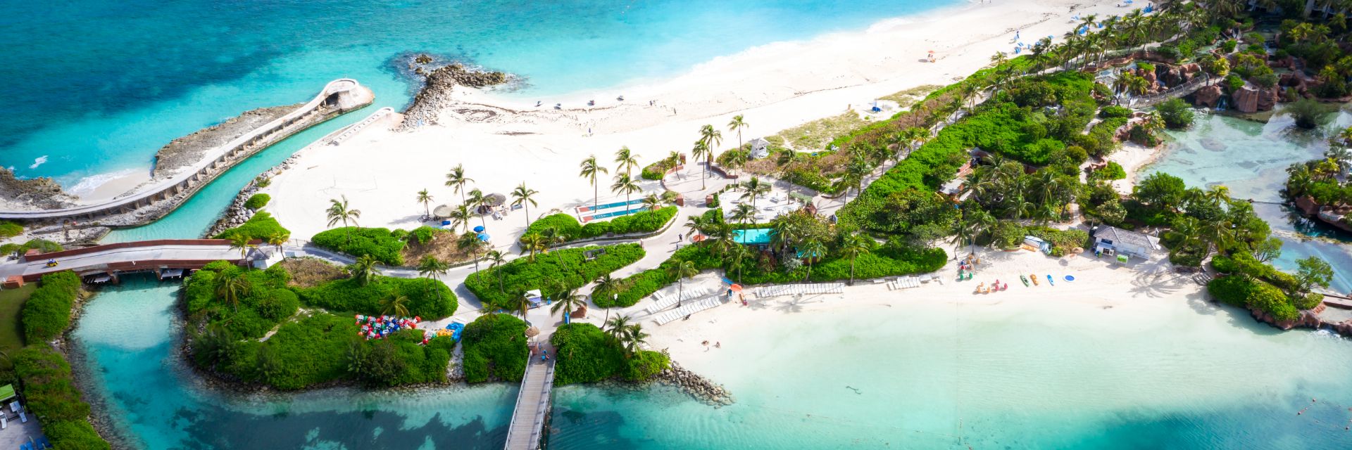 Trees line a sandy beach surrounded by teal blue waters.