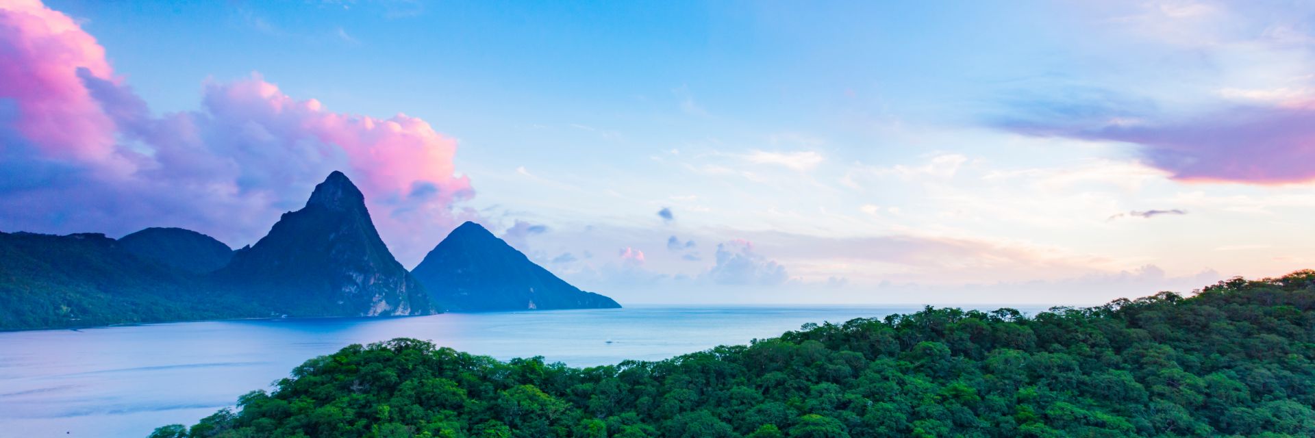 A pastel colored sky sits above a calm waterway dotted with mountains.