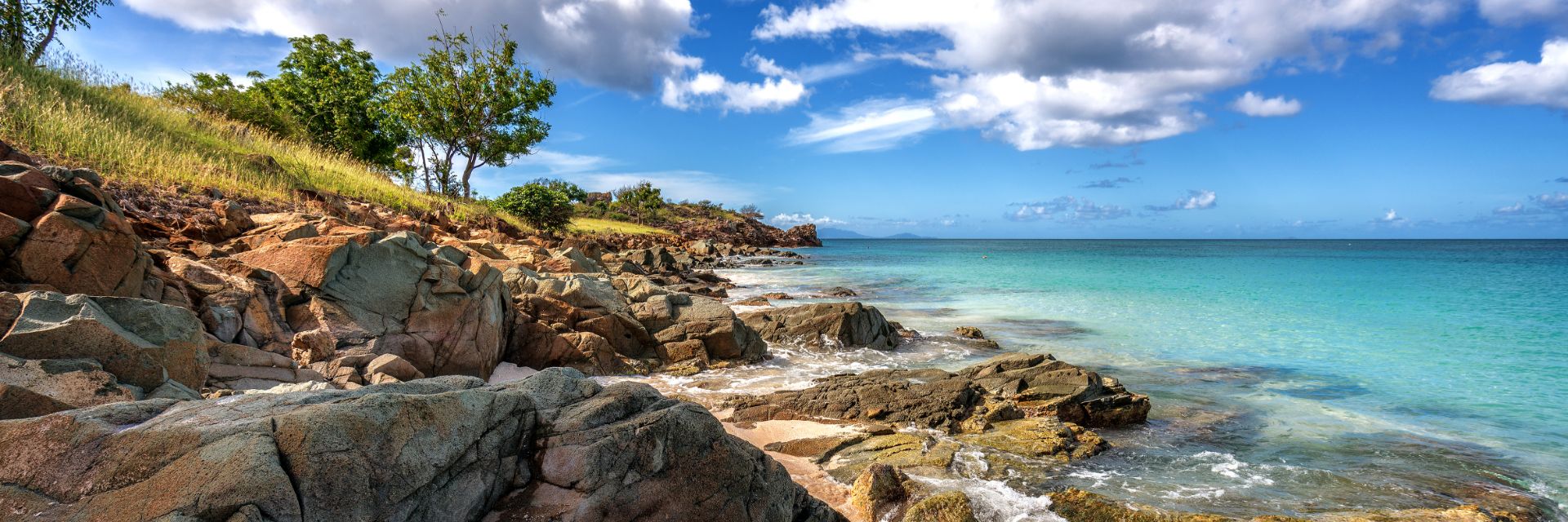 A rocky, grassy coastline meets teal blue waters.