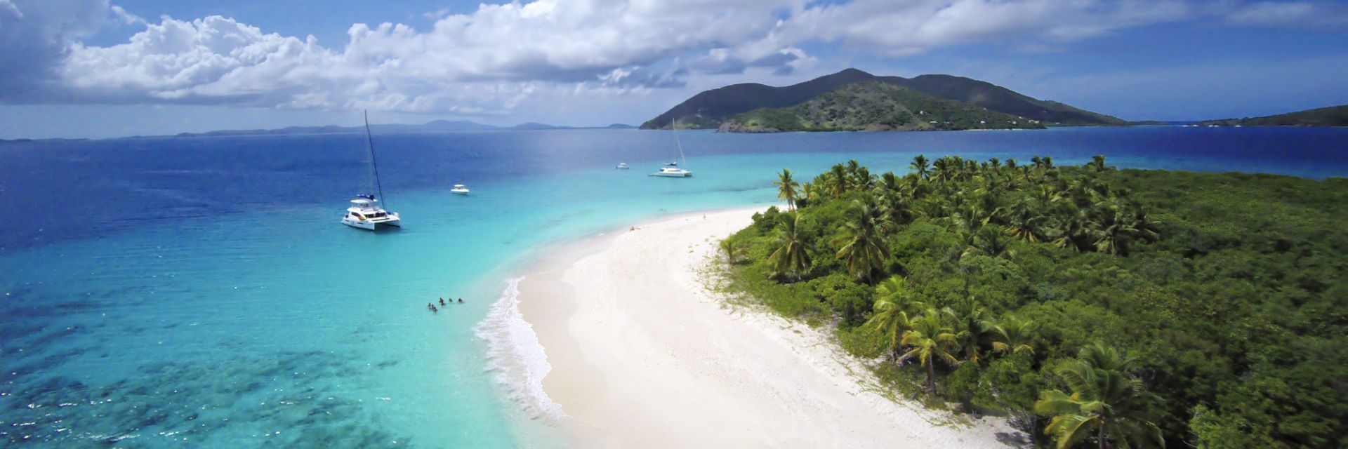 Light blue waters meet a white sandy beach running along a densely populated tree-line.