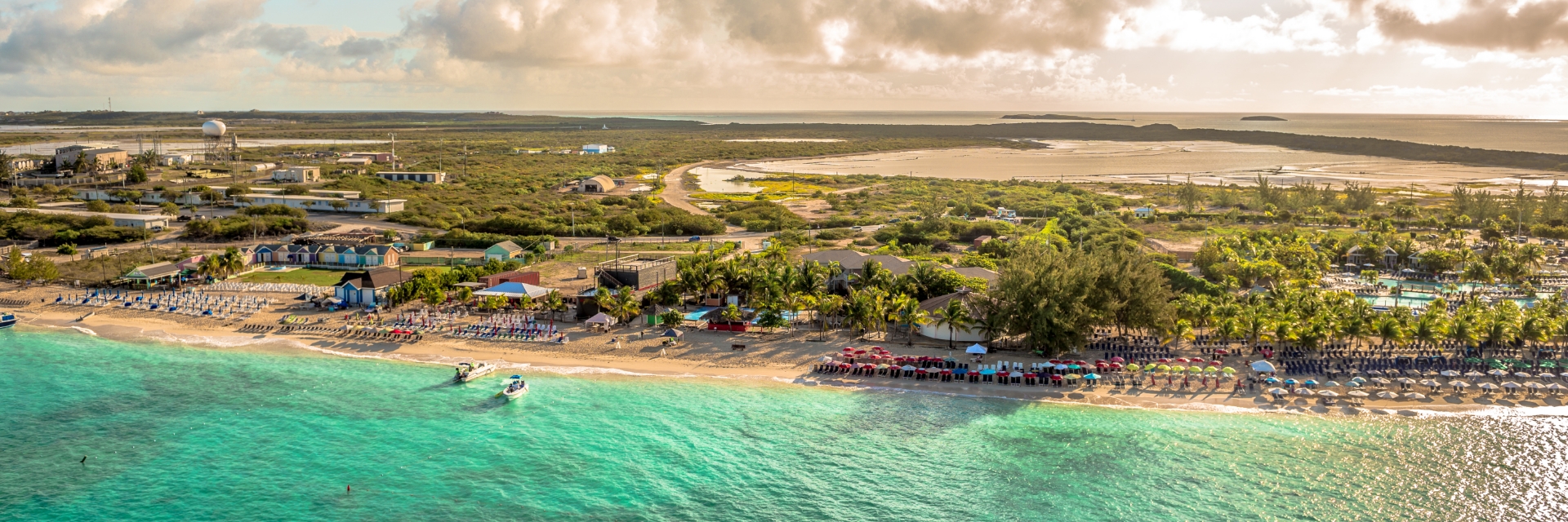 The sun illuminates teal blue ocean waters surrounding a tree-spotted island.