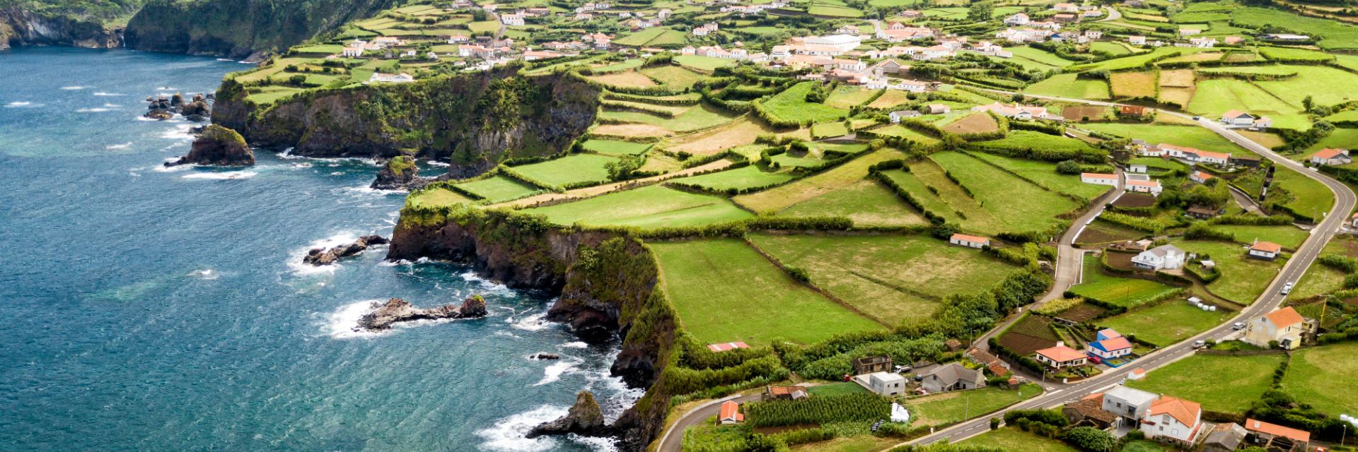 Parcels of bright grass covered land meet a rocky coastline.