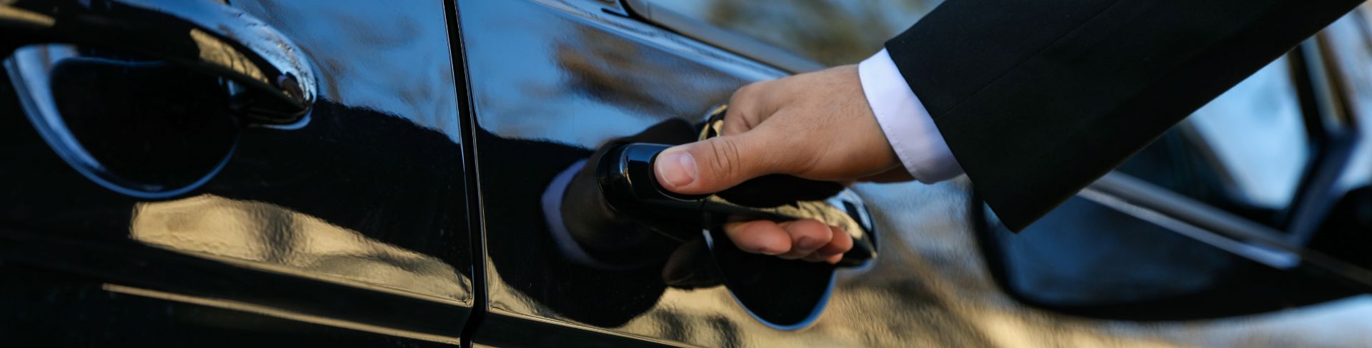 A person in a black suit opens a van door.