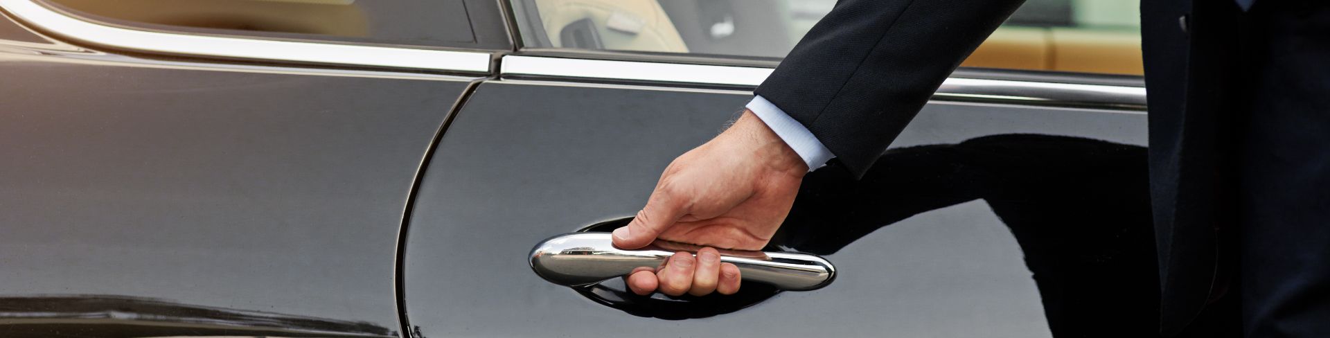 A person in a black suit opens a car door.