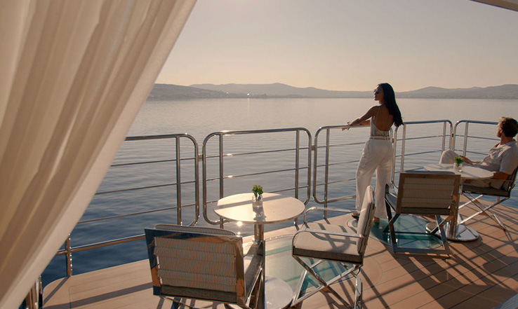 A person stands looking out onto calm seas from their suite balcony.