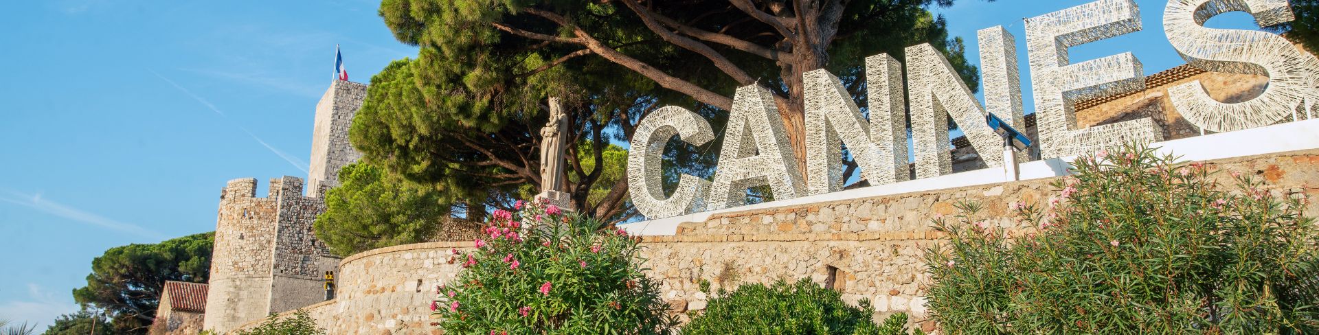 A sign that says "Cannes" sits on rock surrounded by greenery.