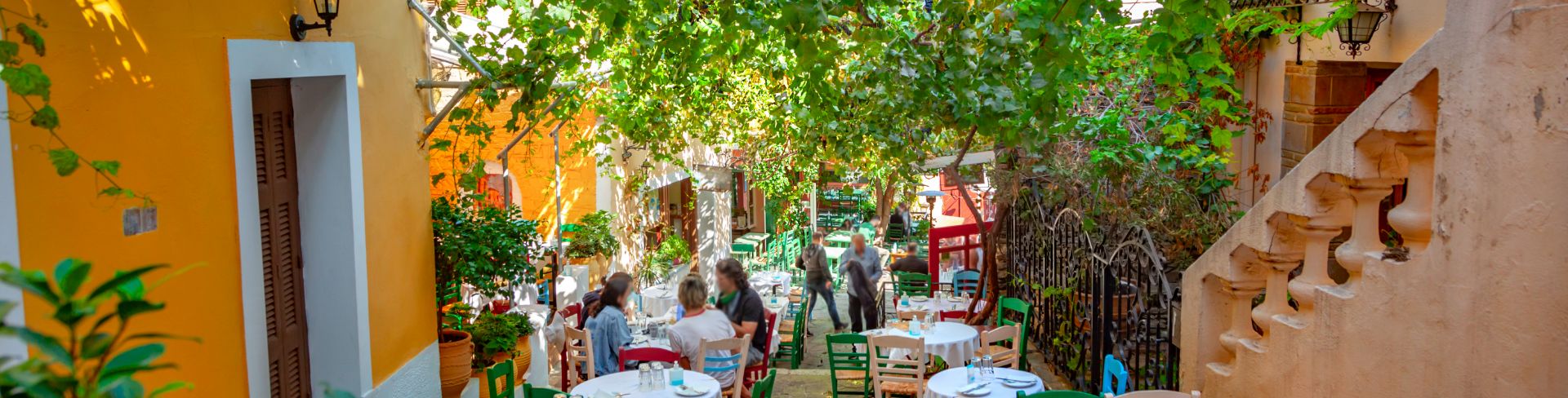 Trees shield a sidewalk filled with dining tables and people.