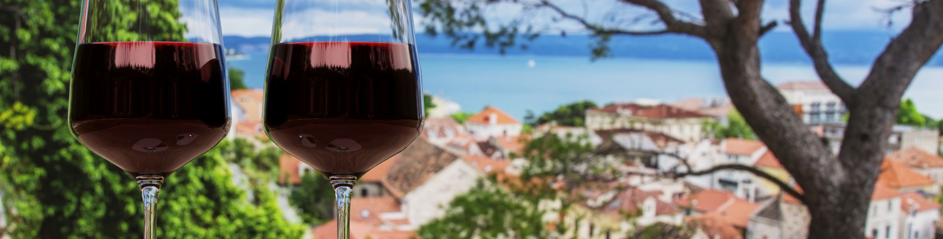 Two glasses of wine sit on a table overlooking terracotta rooftops.