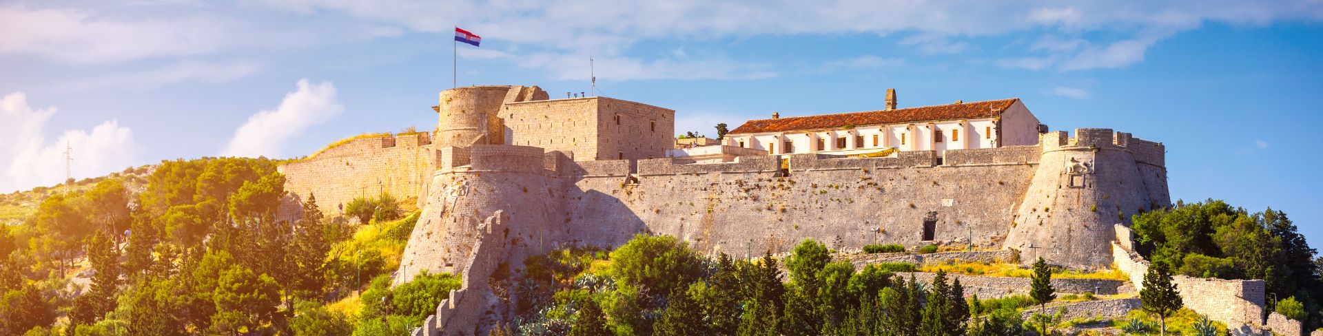The sun illuminates a castle surrounded by trees in Hvar, Croatia.