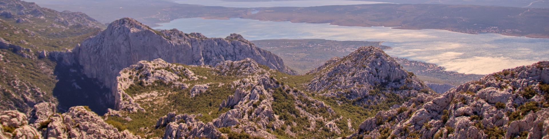 Rocky mountaintops sit before a waterway being illuminated by the sun.