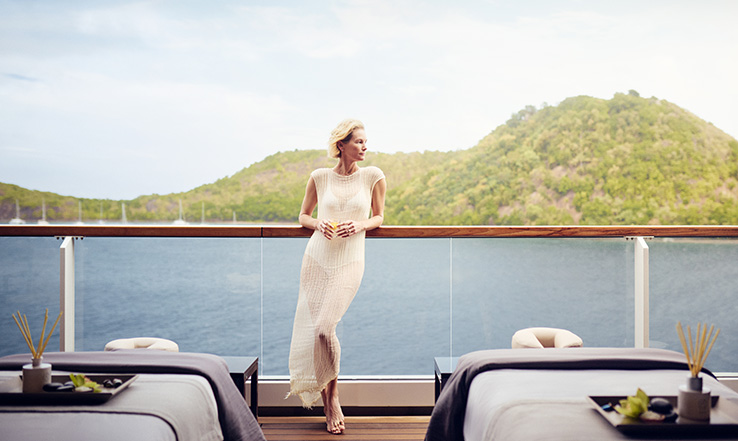 A person leans against a balcony overlooking the ocean.