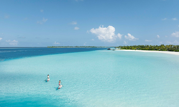 Bright blue waters meet a light sandy beach.
