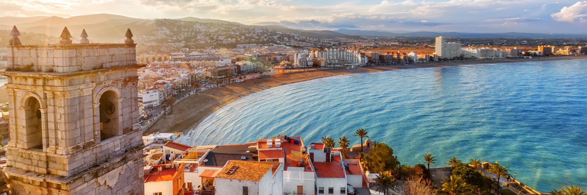 Old buildings and white and orange homes cover the shoreline that opens up to bright blue water.
