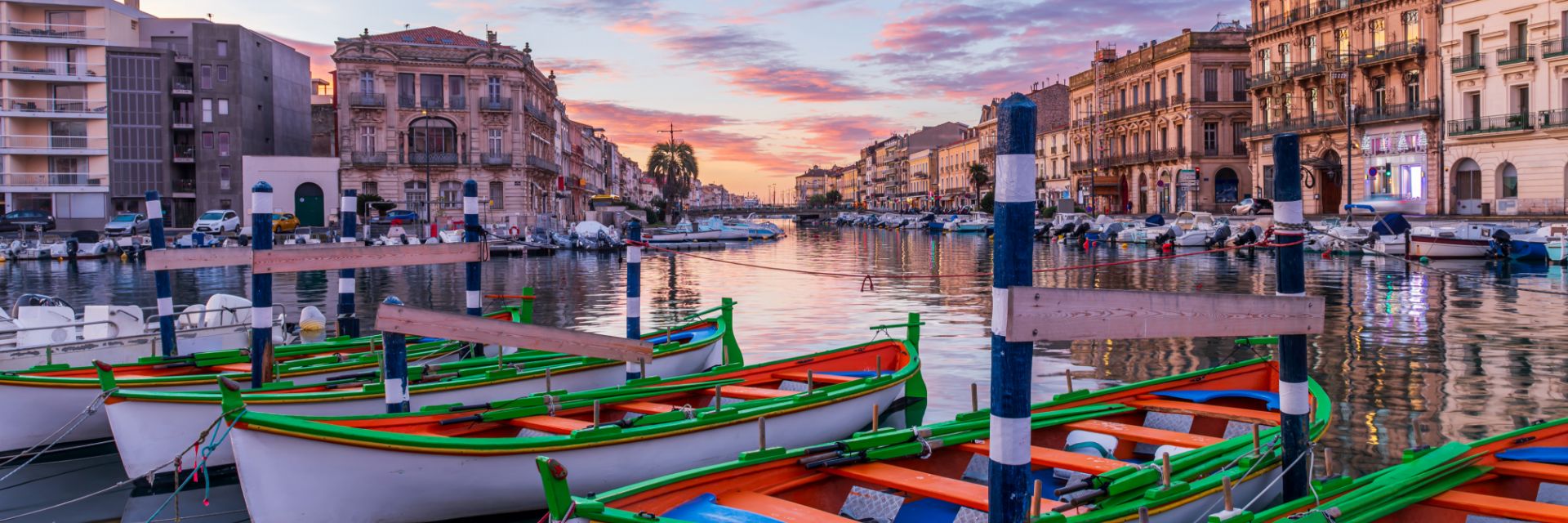 Colorful boats line a waterway with large stone buildings in the background.