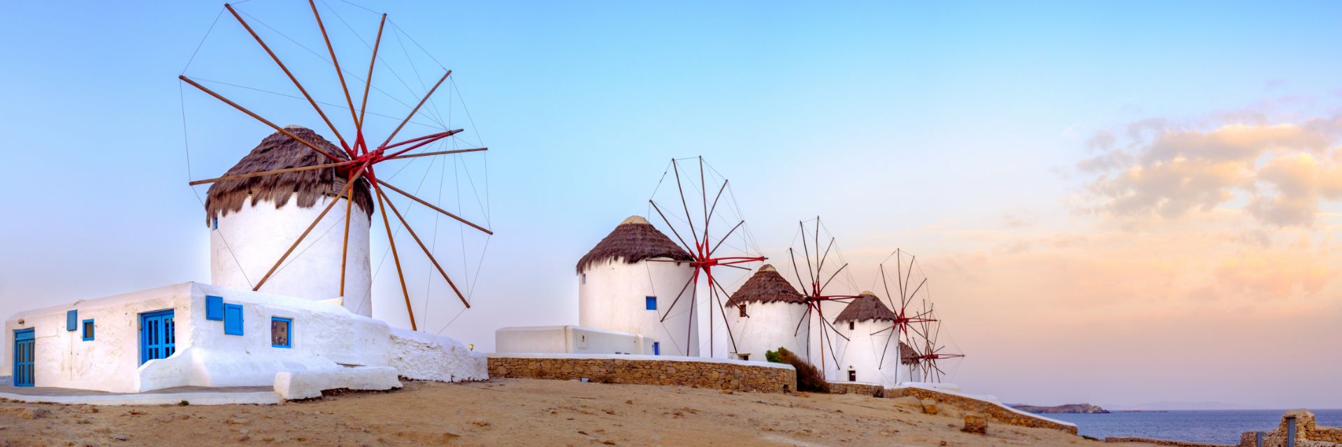 The sun illuminates the sky behind three windmills.