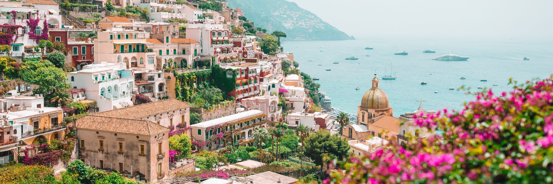Buildings climb a mountainside with light blue waters in the background. 