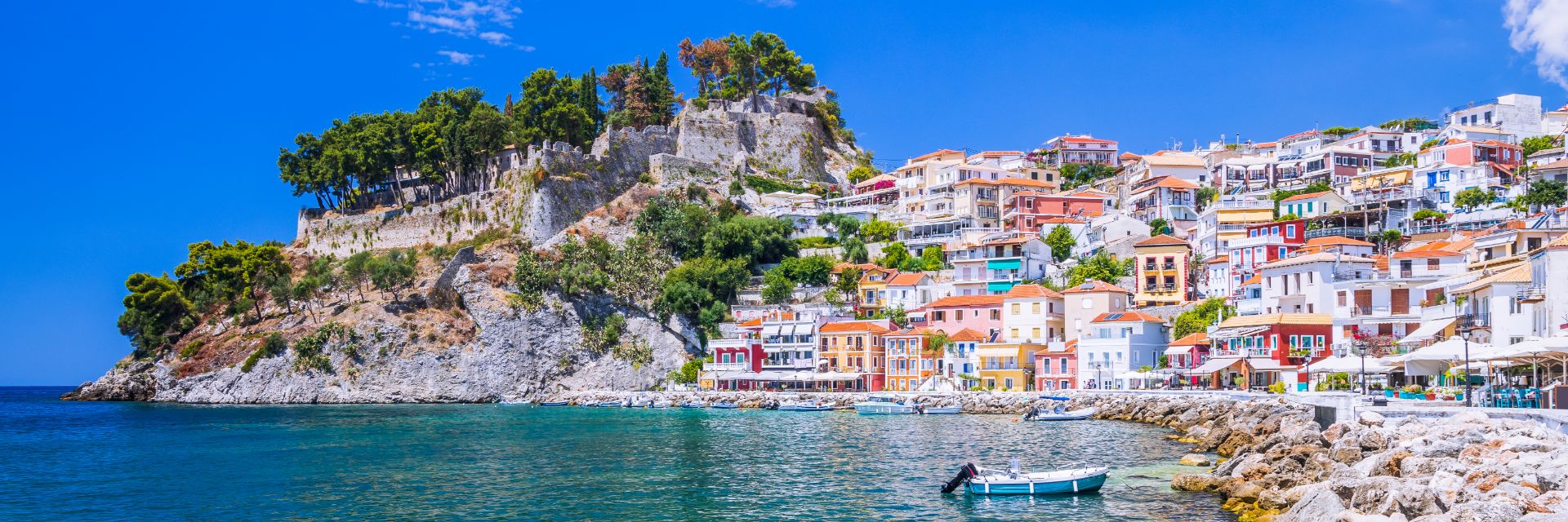 Pastel colored buildings climb a mountainside overlooking the ocean.