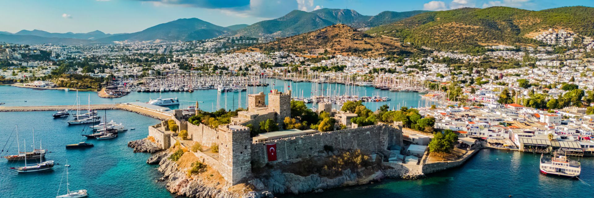 A castle sits out on an island in a harbor lined with boats.