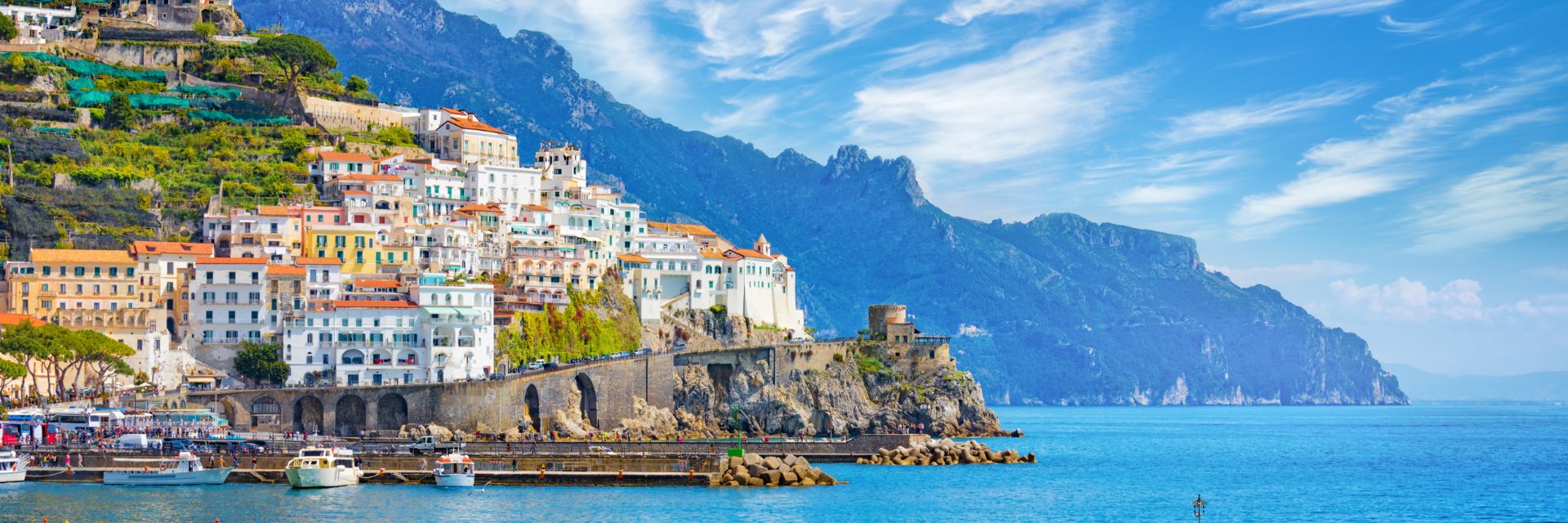 Buildings climb a mountainside overlooking deep blue ocean waters. 