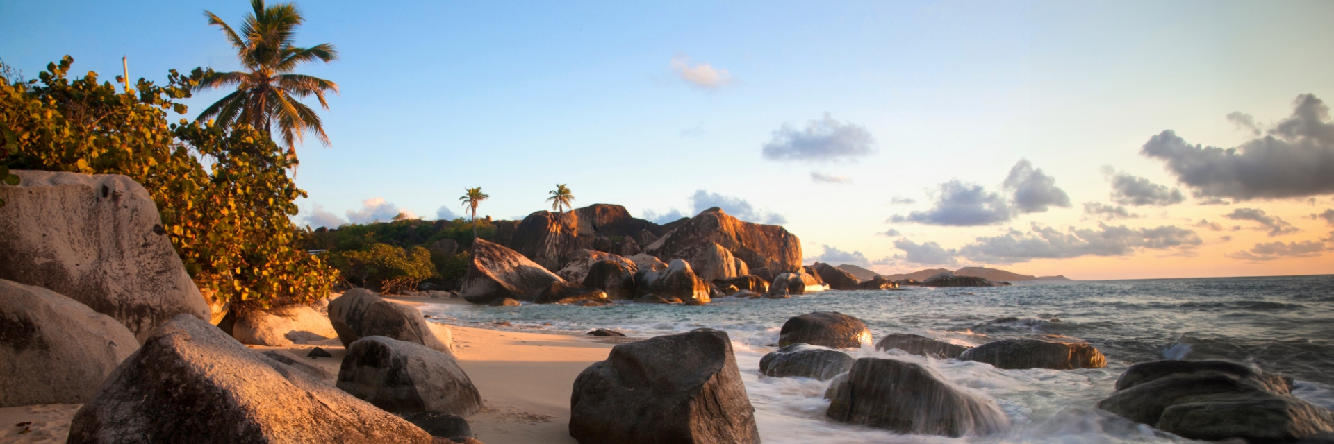 Smooth rocks sit on a sandy beach with the sunset in the background.