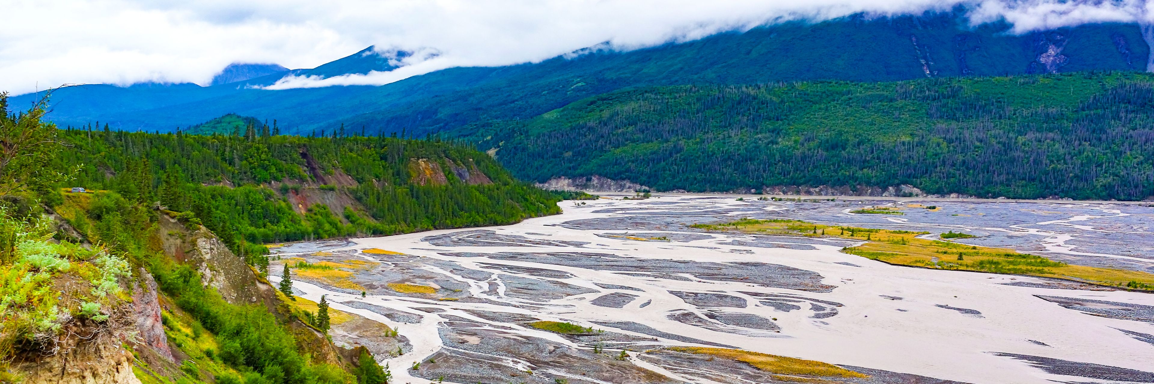 A multicolored waterway sits surrounded by tree covered mountains.