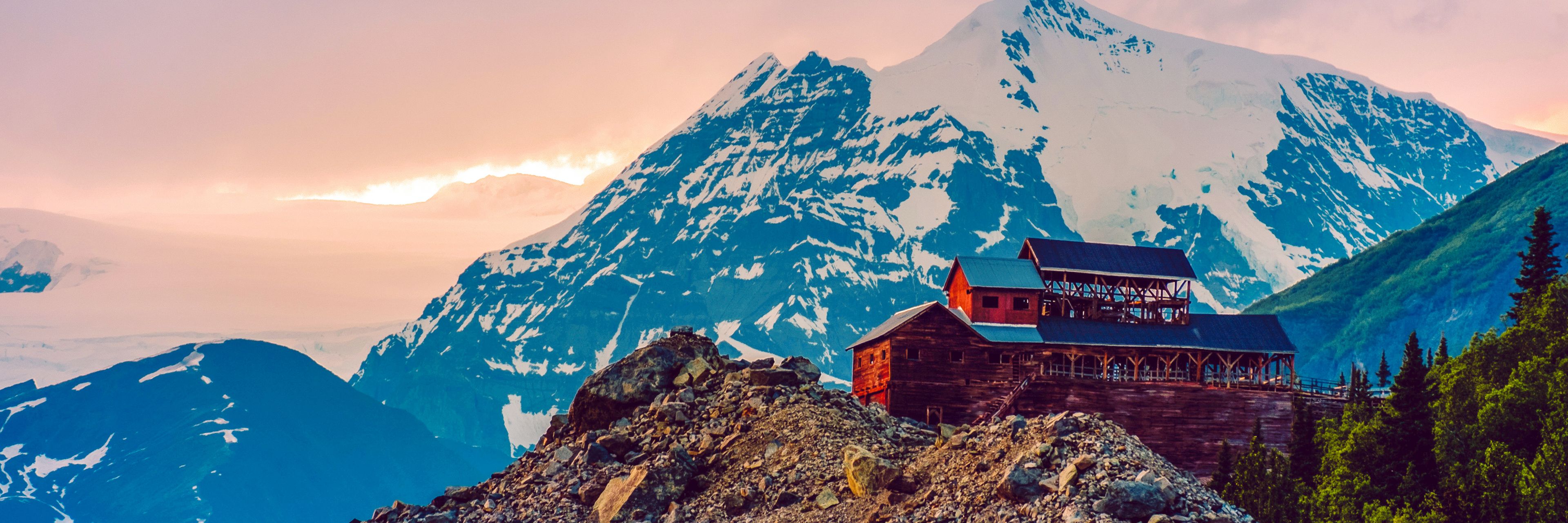 A small red buildings sits atop a mountain peak with a larger mountain sitting behind it.