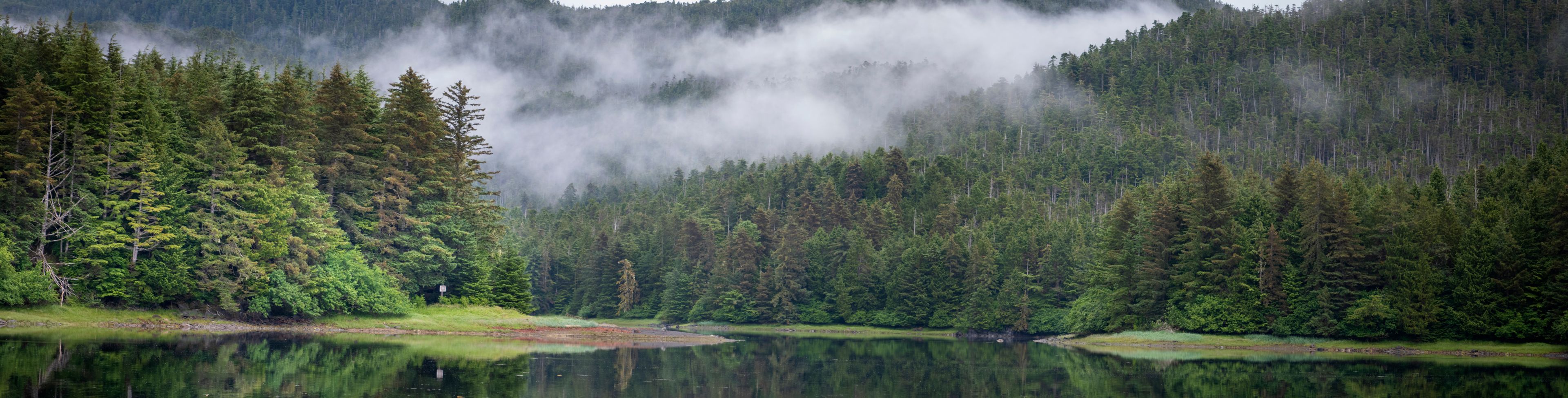 Clouds hover over mountains and a still waterway.