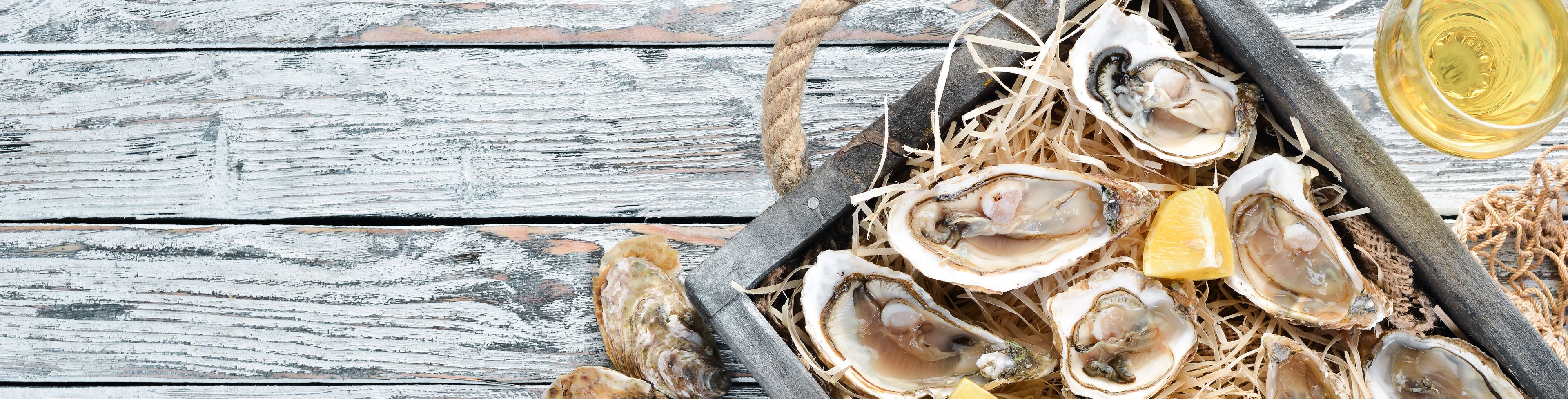 Oysters sit prepared on a platter with lemon wedges.