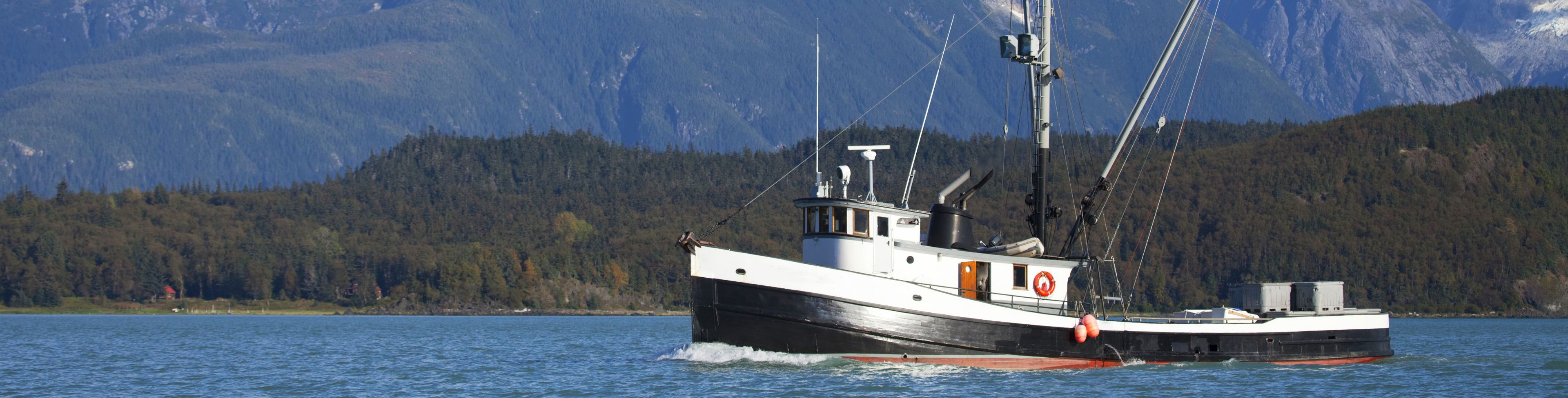 A fishing boat floats through deep blue waters in front of snow capped mountains.