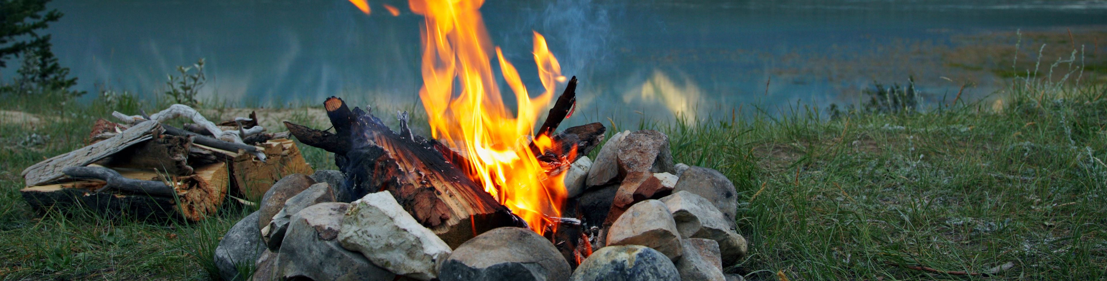 A fire burns before a waterway sitting in front of a mountain.