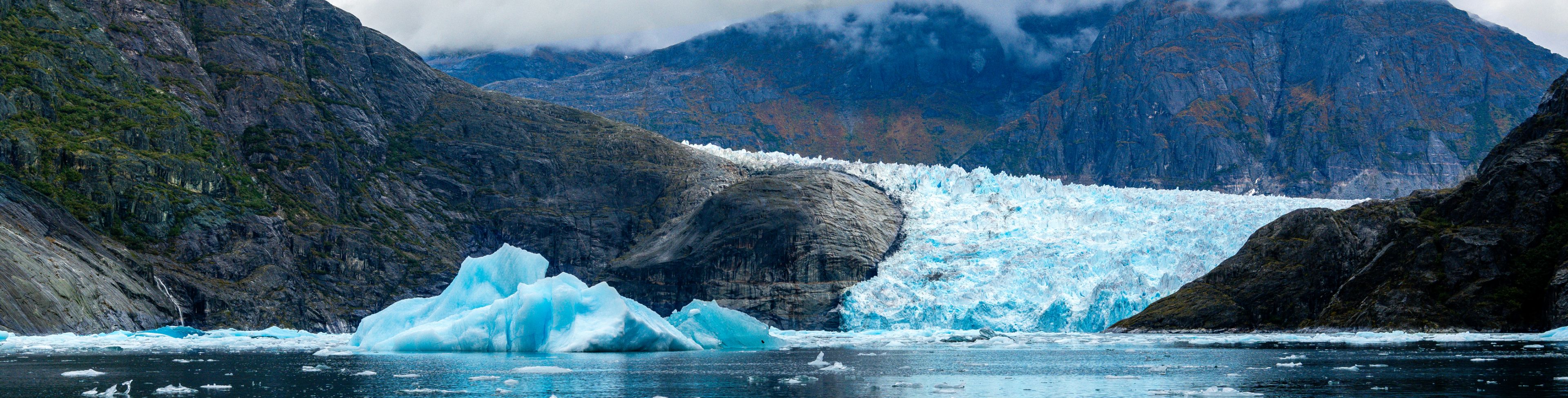 Ice floats through deep blue waters in front of small mountains.