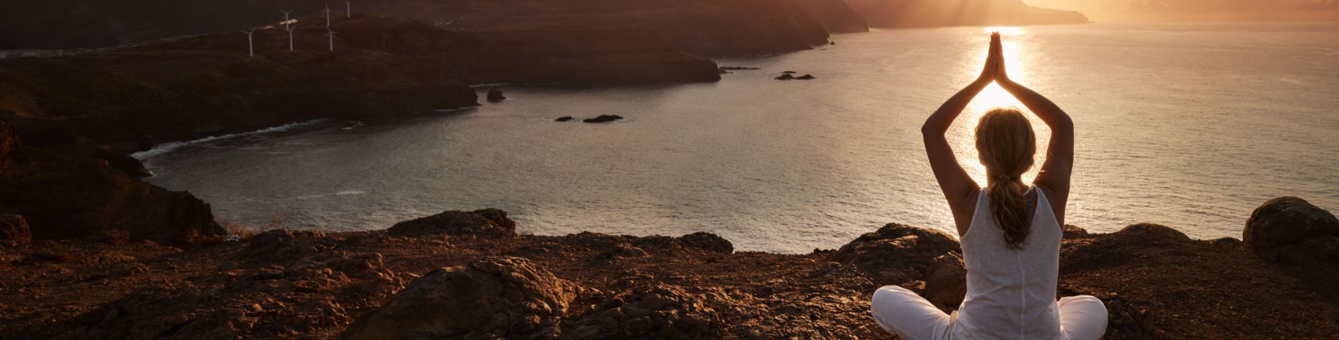 Woman doing yoga on a cliff during sunrise.