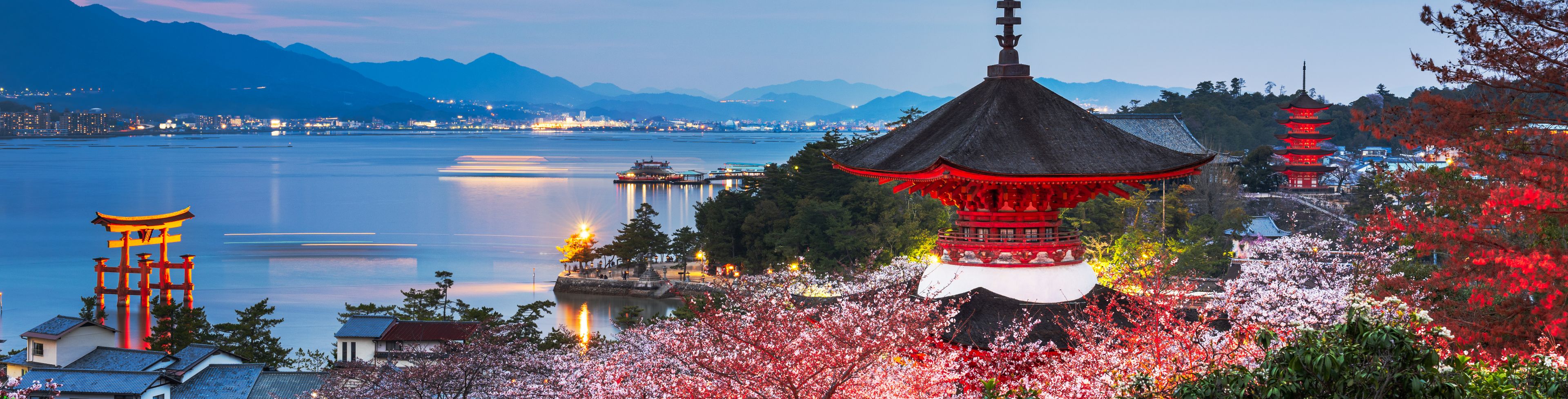 Miyajima during dusk, red and green trees surrounding temple building. 
