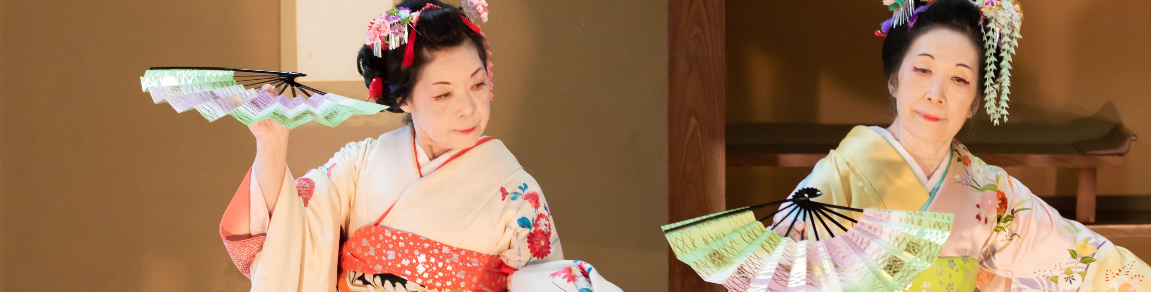 Two women dressed traditionally with fans, while dancing. 
