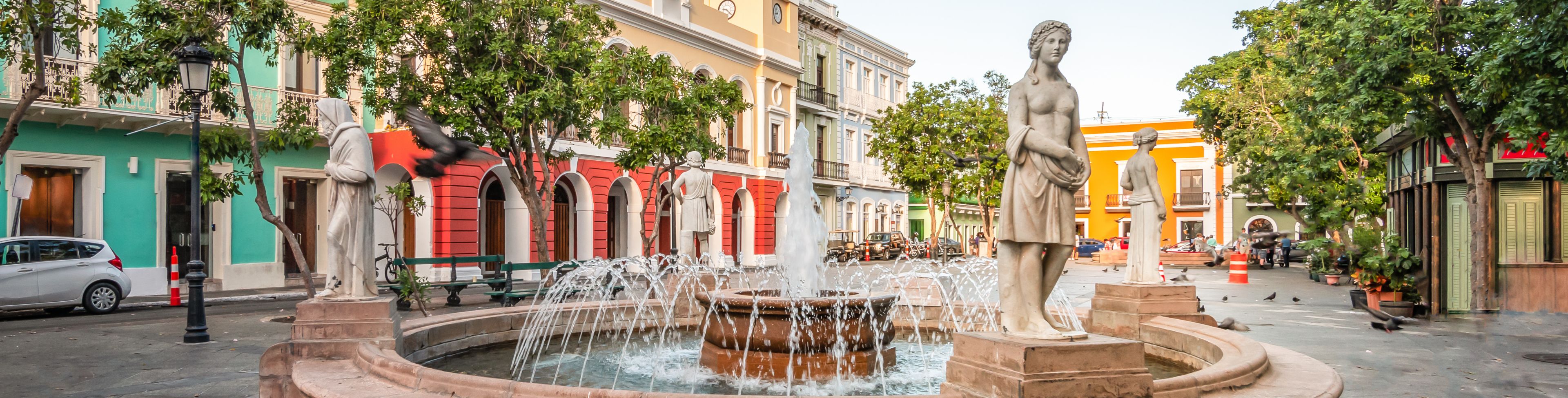 Large fountain surrounded by buildings and trees. 