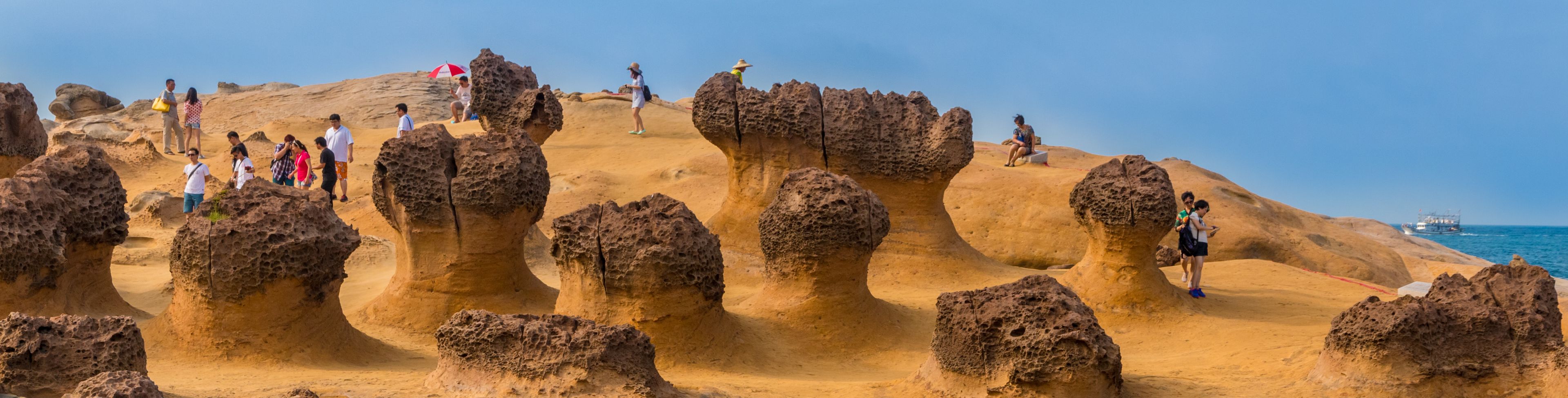 Rock and sand formations on dry land, people walking and looking at the formations. 