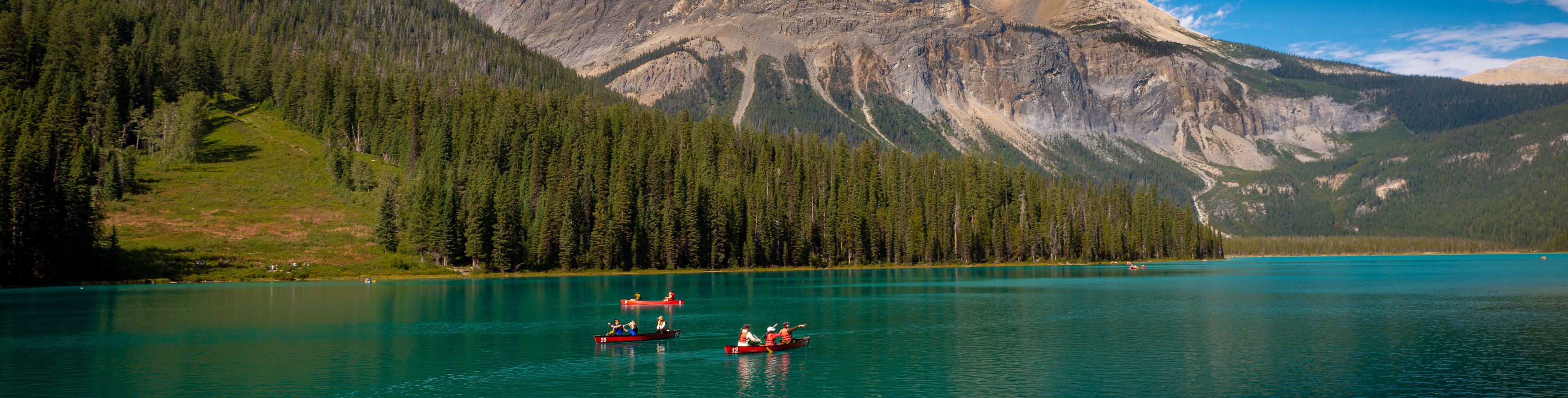 Two boats on green-blue water, surrounded by mountains and trees. 
