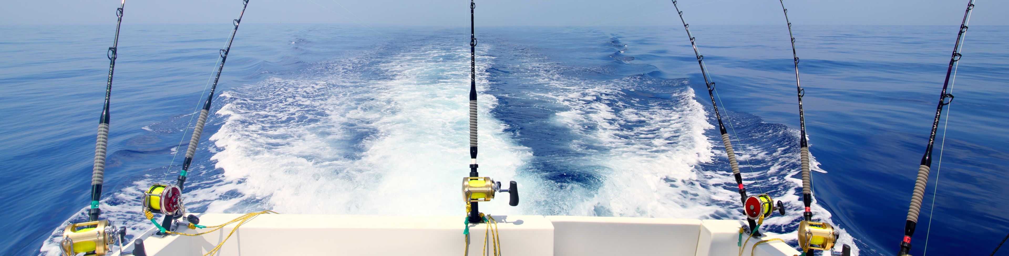 Three fishing poles attached to the back of a moving boat. 