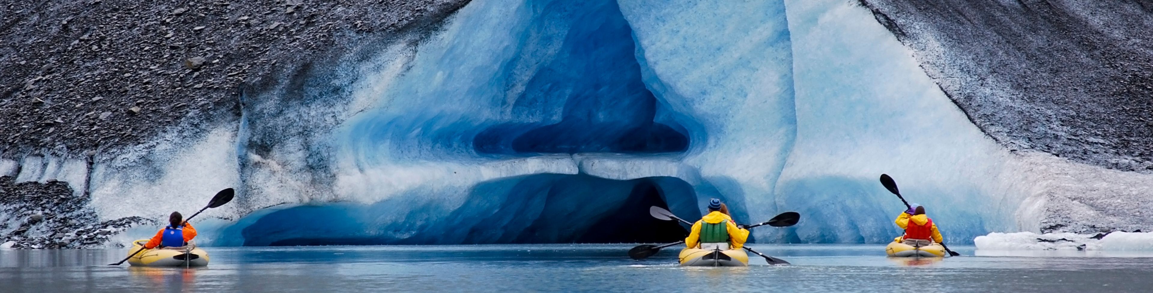 Three kayaks kayaking near glacier at the edge of the water.
