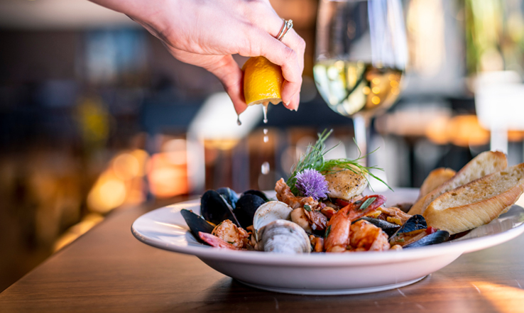 Someone squeezing a lemon on top of a plate of seafood and bread. 