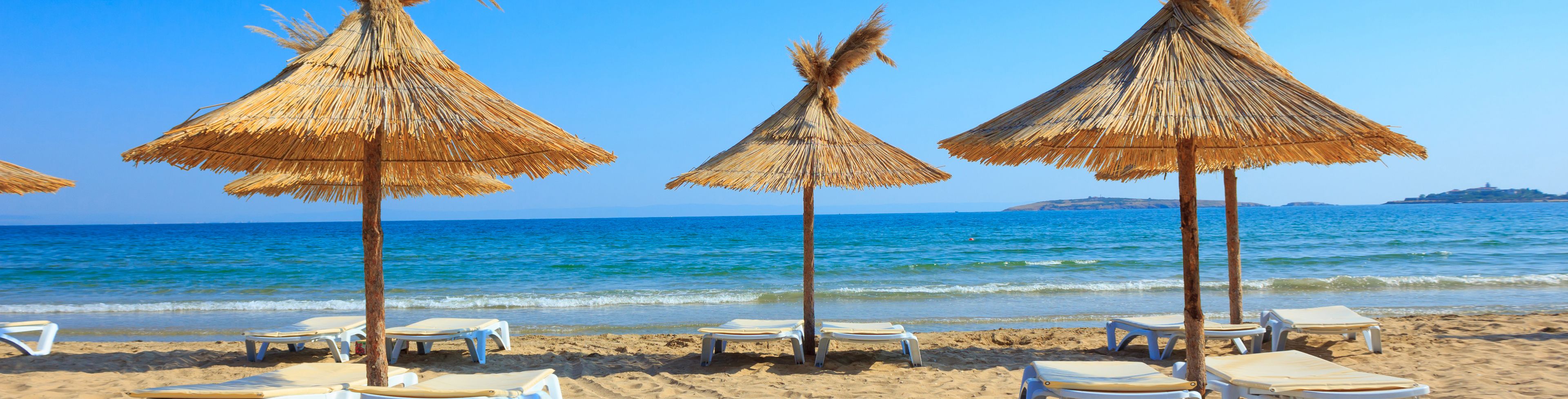 Straw umbrellas over lounge chairs on a sandy beach. 