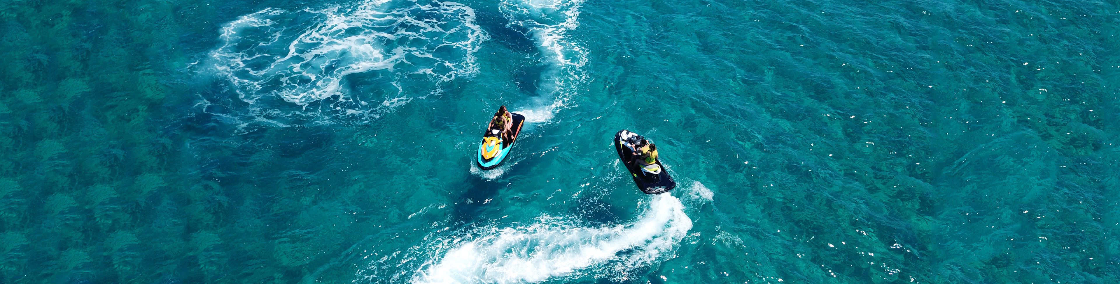 Two people on two jet skis driving on the water around each other. 