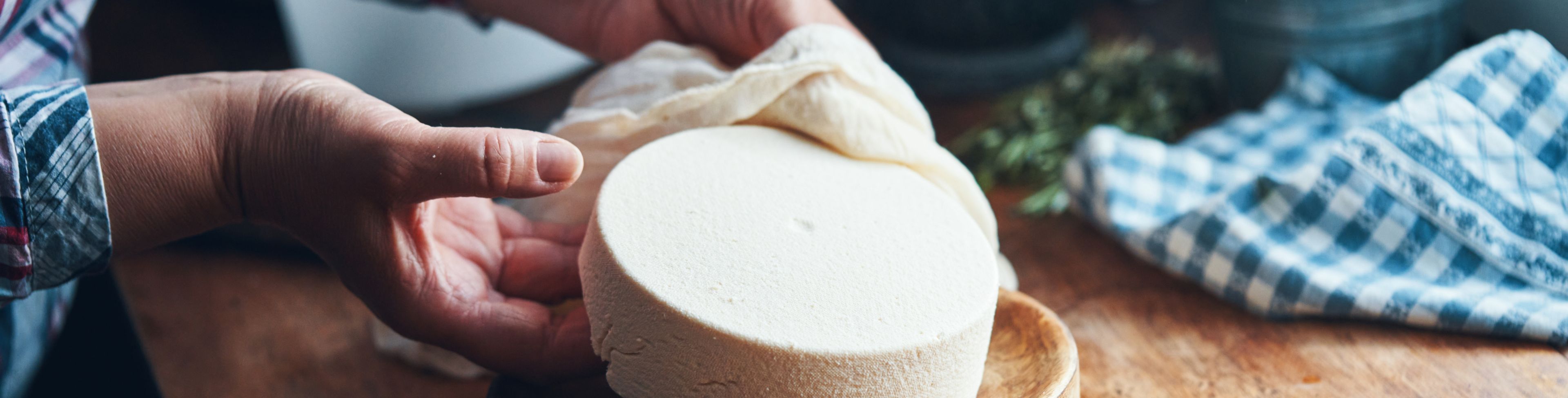 Someone putting a cheese wheel on a wooden plate. 