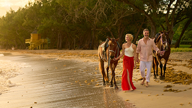 People walking with horses on the beach. 