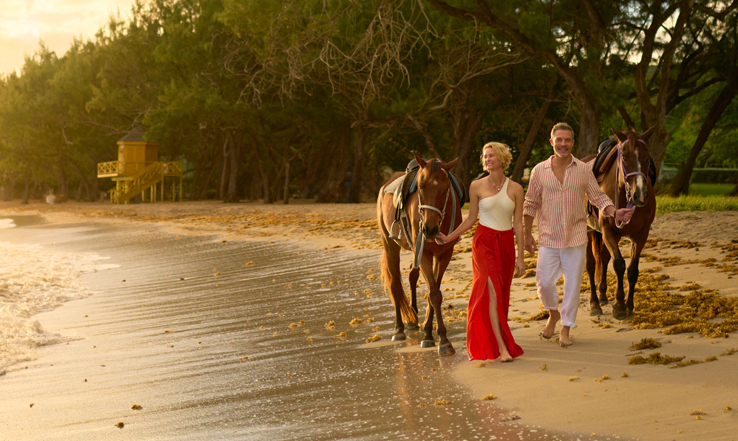People walking with horses on the beach. 