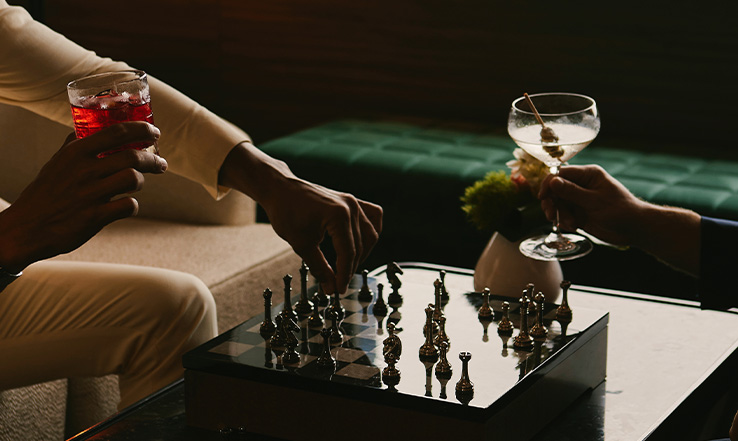 Two people playing chess with cocktails in their hands. 