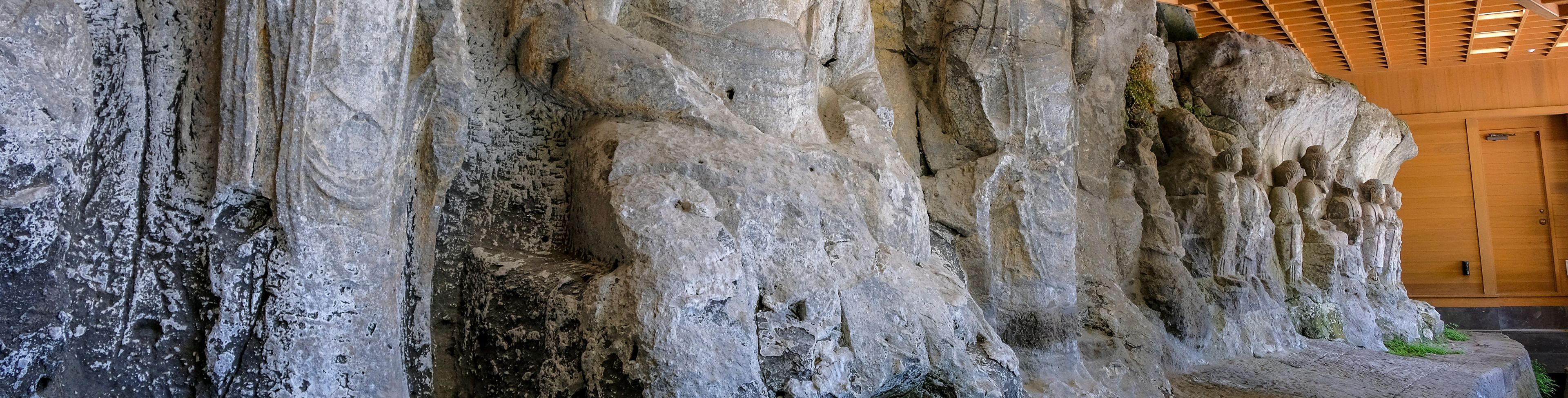 Multiple budda statues carved into a stone rock wall. 