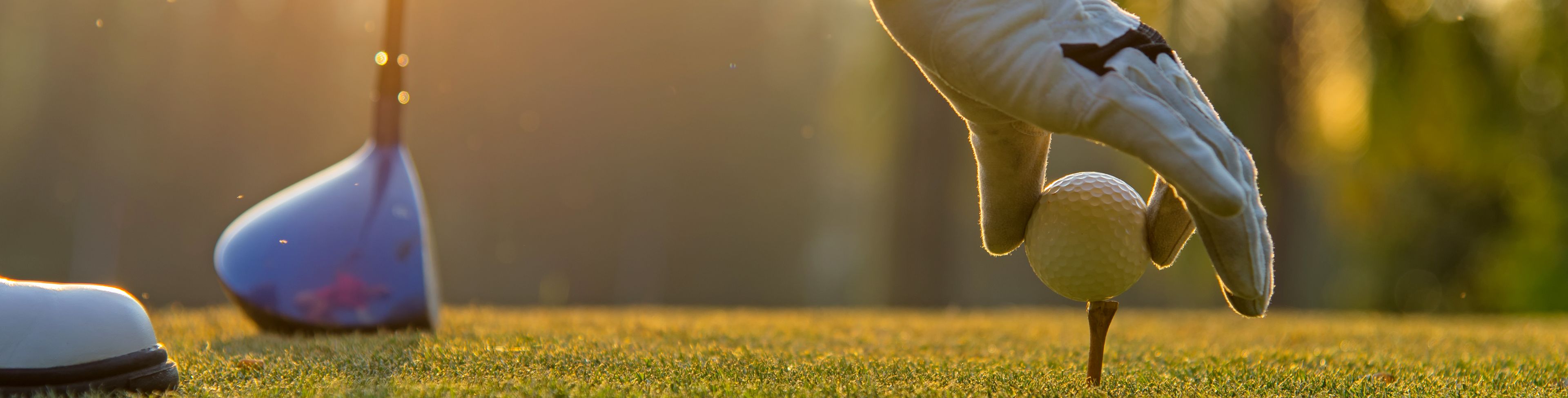 Person holding a golf ball on a tee that is in the ground. 